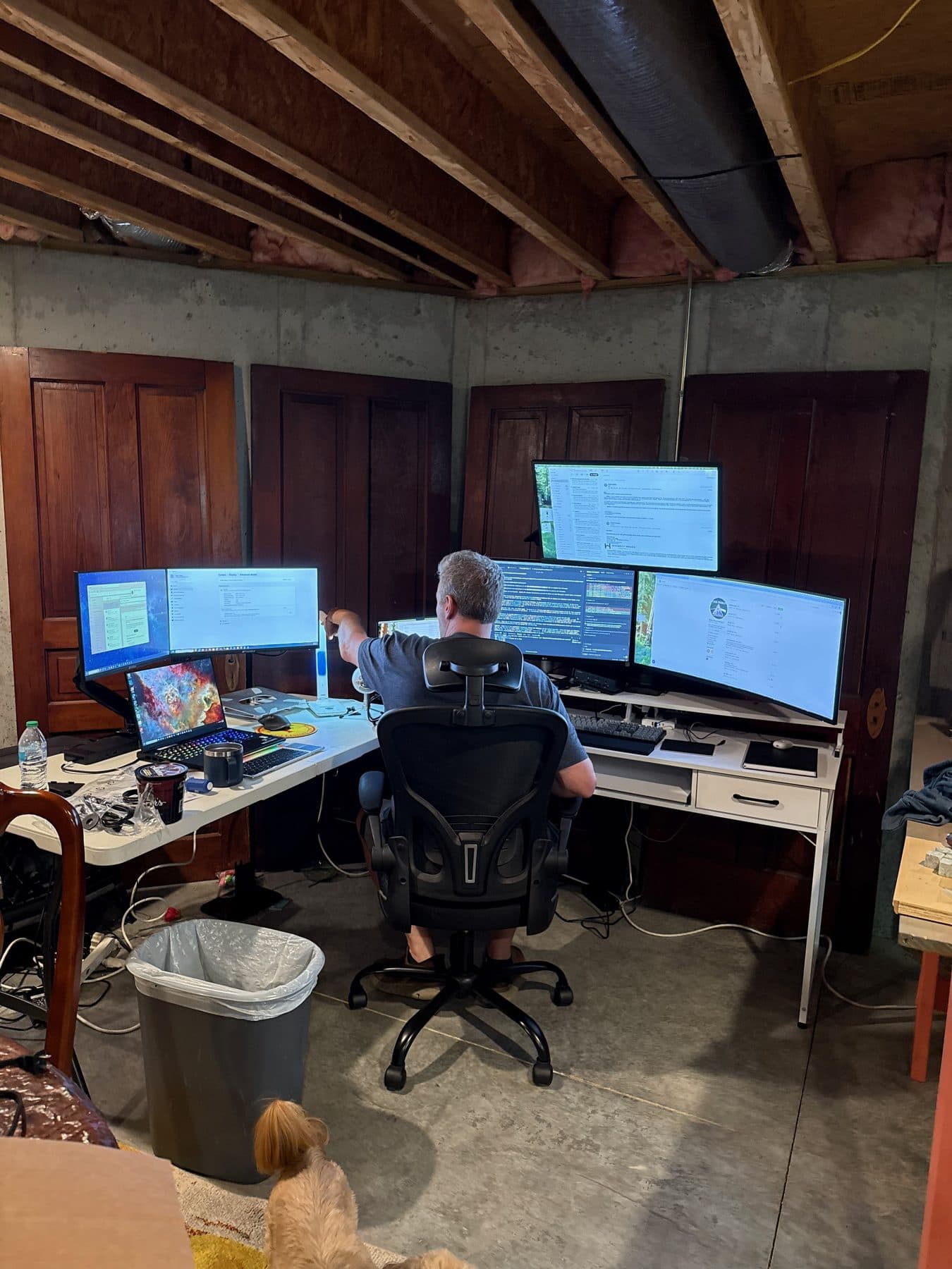 A multi-monitor engineering workstation in a home office. A goldendoodle sits underfoot.
