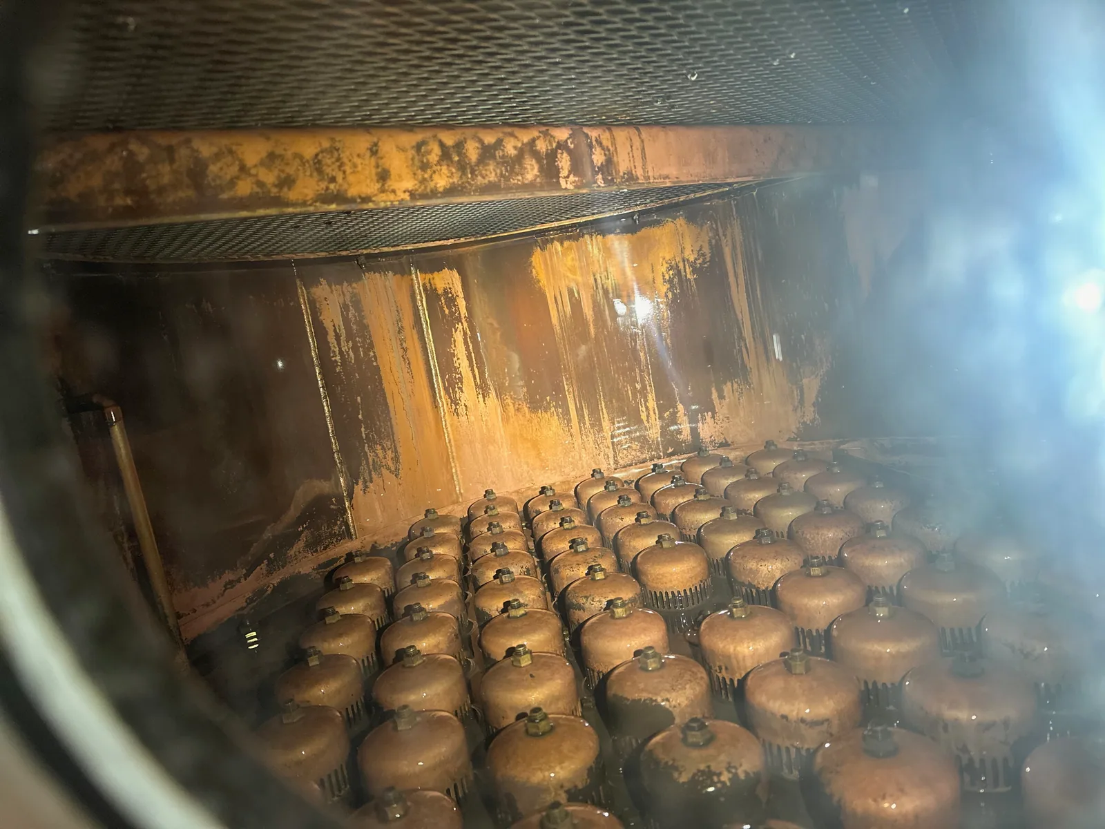 Close-up looking down into a copper distillation column showing the bubble-cap tray and its risers.